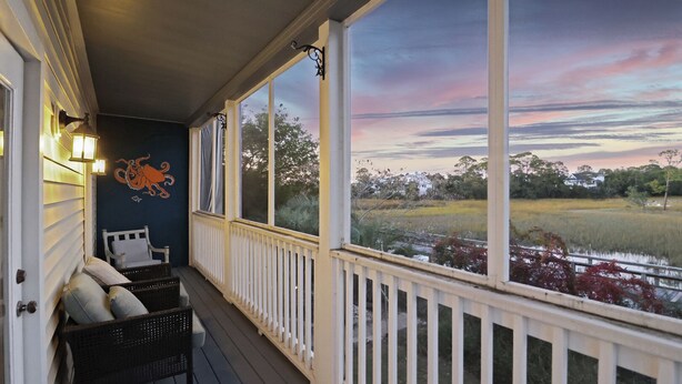 A porch with a view of a sunset over a field, a chair, and a wall mural.