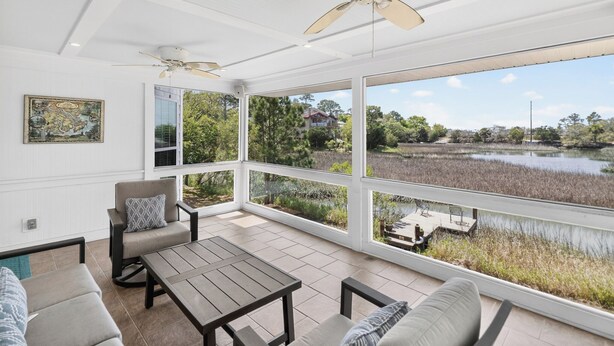 Une véranda avec vue sur un lac, un ventilateur de plafond et une table avec des chaises.