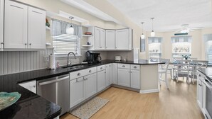 Une cuisine moderne avec des meubles blancs, un plan de travail noir et un coin repas comprenant une table et des chaises.