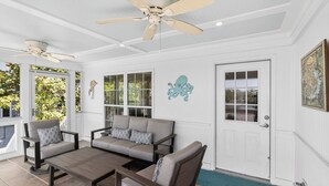 Une véranda avec un ventilateur de plafond, un canapé, un fauteuil et une table basse.