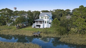Une maison à deux étages avec une jetée qui s’avance dans un plan d’eau, le tout entouré d’une végétation luxuriante.