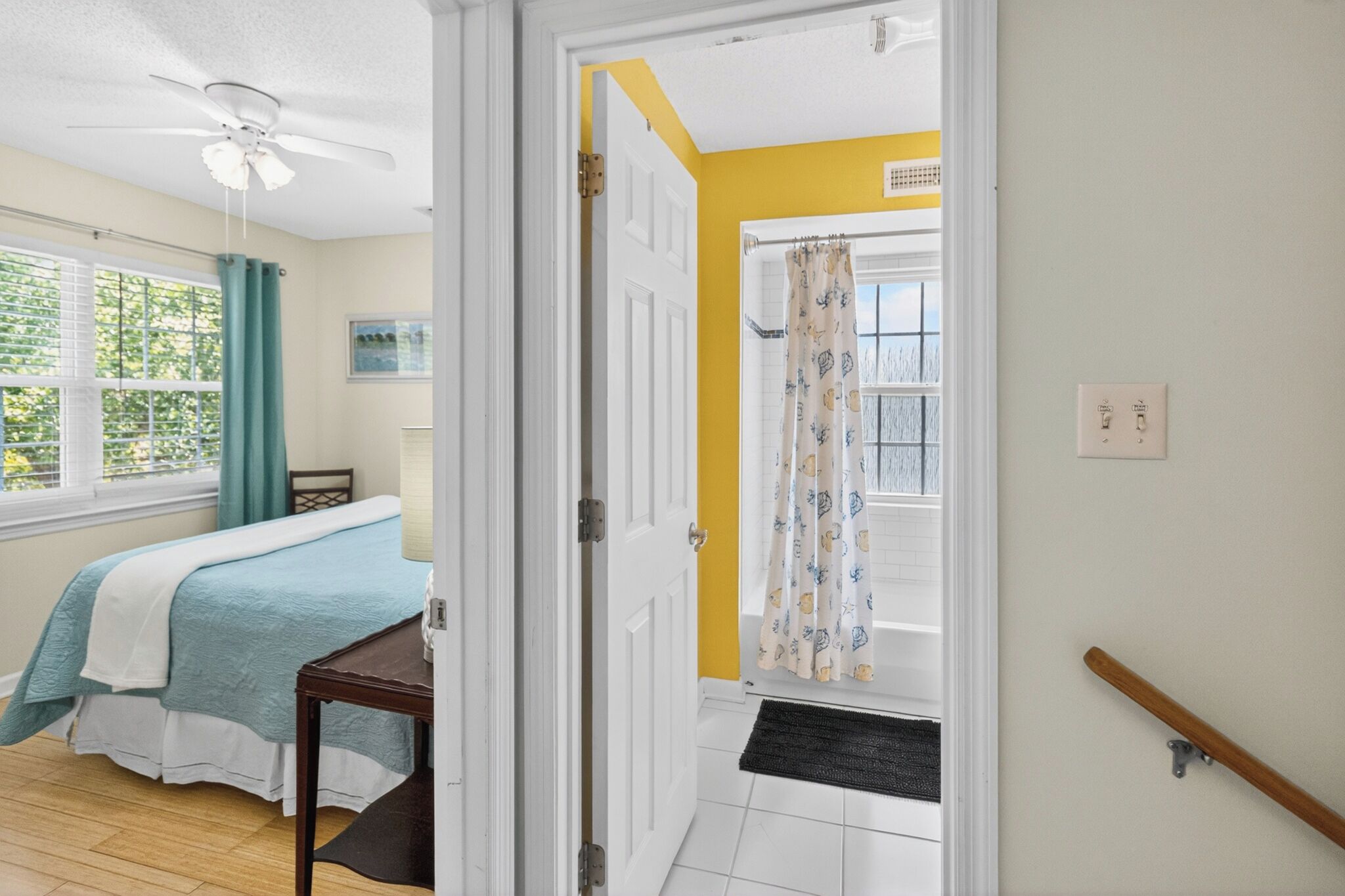 A bedroom with a bed, a desk, a ceiling fan, a window with curtains, and a door leading to a balcony.