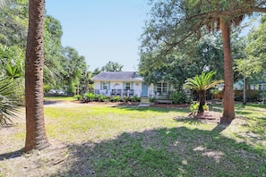 A house with a front yard, surrounded by trees and a fence. - Palmwood Paradise | Fire Pit Nights + Family-Friendly Stay (Tybee Island)