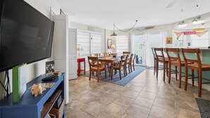 A modern living room with a flat-screen TV, dining table, chairs, and a ceiling fan. - Steps to the Beach | Ocean Glimpses from the Balcony (Tybee Island)
