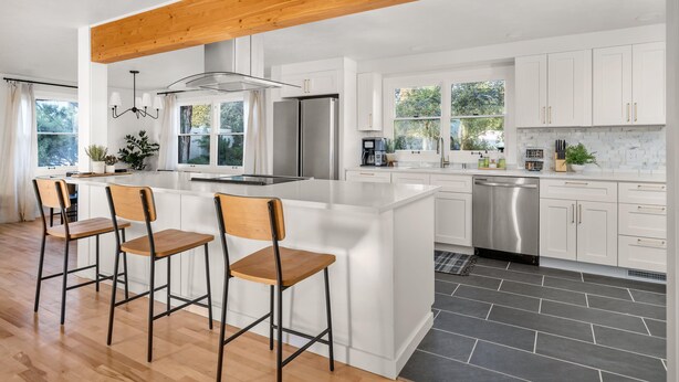 Une cuisine moderne avec des meubles blancs, un îlot central doté de tabourets de bar, un réfrigérateur en acier inoxydable et un lave-vaisselle.