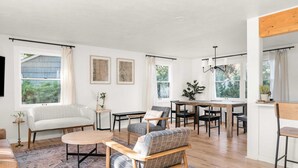 Un salon spacieux comprenant un canapé, des fauteuils, une table à manger et un tapis. De nombreuses fenêtres laissent entrer la lumière naturelle et offrent une vue sur la verdure environnante.