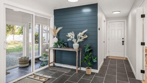 Un hall d’entrée moderne avec un mur foncé, une console en bois et une plante en pot.