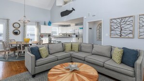 A modern living room with a gray sectional sofa, a wooden coffee table, and a dining area with a wooden table and chairs.
