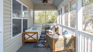 A covered porch with a ceiling fan, a wooden table with chairs, and a view of trees through the windows.