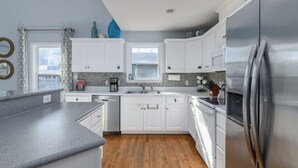 A modern kitchen with white cabinets, a stainless steel refrigerator, and a wooden floor.