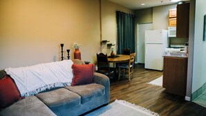 A compact living space with a sofa, dining table, chairs, a kitchen area with a refrigerator and stove, and a window with curtains.