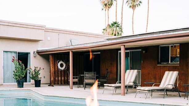 A pool area with a fire feature, lounge chairs, and palm trees.