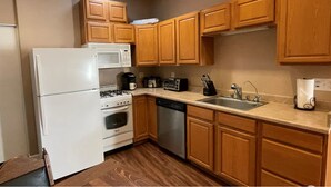 A compact kitchen with wooden cabinets, a white refrigerator, a microwave, a stove, a dishwasher, and a coffee maker.