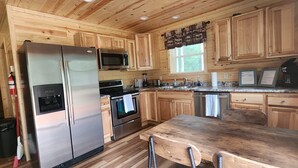 Une cuisine rustique aménagée dans une cabane en bois, équipée d’un réfrigérateur, d’un four à micro-ondes, d’un four et d’un lave-vaisselle, tous en acier inoxydable.