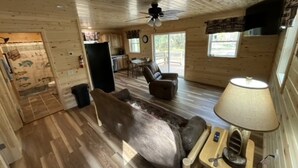 L'intérieur d'une cabine avec un plancher en bois, un canapé, un fauteuil, une lampe et un ventilateur de plafond.