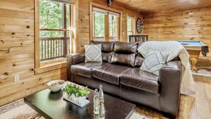 A wooden cabin interior with a leather sofa, a coffee table with a bowl and bottles, and a dartboard. - Mtn Views | Sleeps 8, Hot Tub | Pool & Tennis (Sevierville)