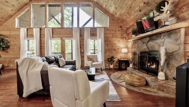 A cozy cabin interior with a stone fireplace, a leather sofa, and a television mounted on the wall. - Mtn Views | Sleeps 8, Hot Tub | Pool & Tennis (Sevierville)