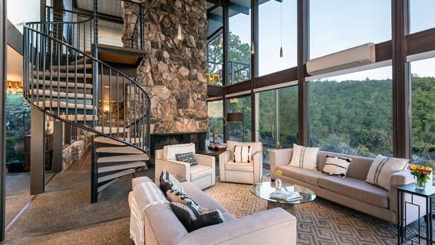 A modern interior with a stone fireplace, a spiral staircase, and large windows offering a forest view. - 7 BD - 2 homes - Pool, Spa, Minutes to Plaza (Sonoma)