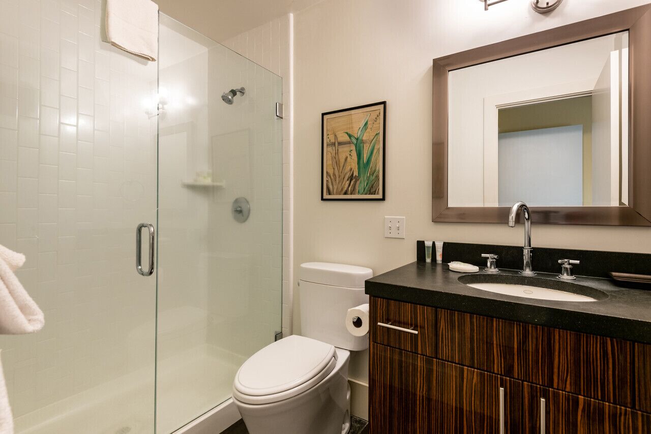Un baño moderno con cabina de ducha de vidrio, inodoro, lavabo con espejo y muebles de madera.