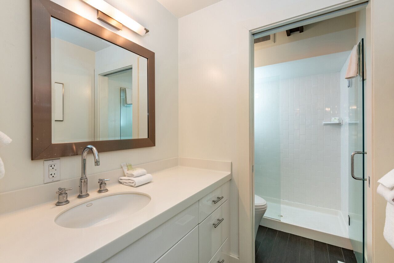 Une salle de bain moderne avec un grand miroir, un lavabo et une douche à parois de verre.