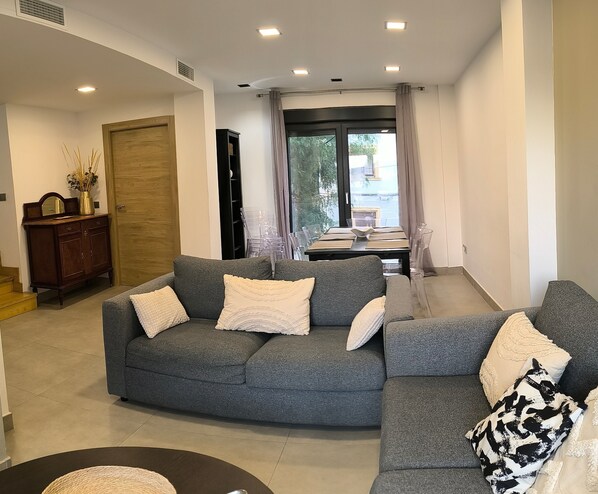 A modern living room with a grey sectional sofa, a wooden cabinet, and a dining area with a table and chairs.