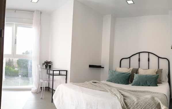 Un dormitorio con una cama, una mesita con una planta, una silla y una ventana con cortinas.