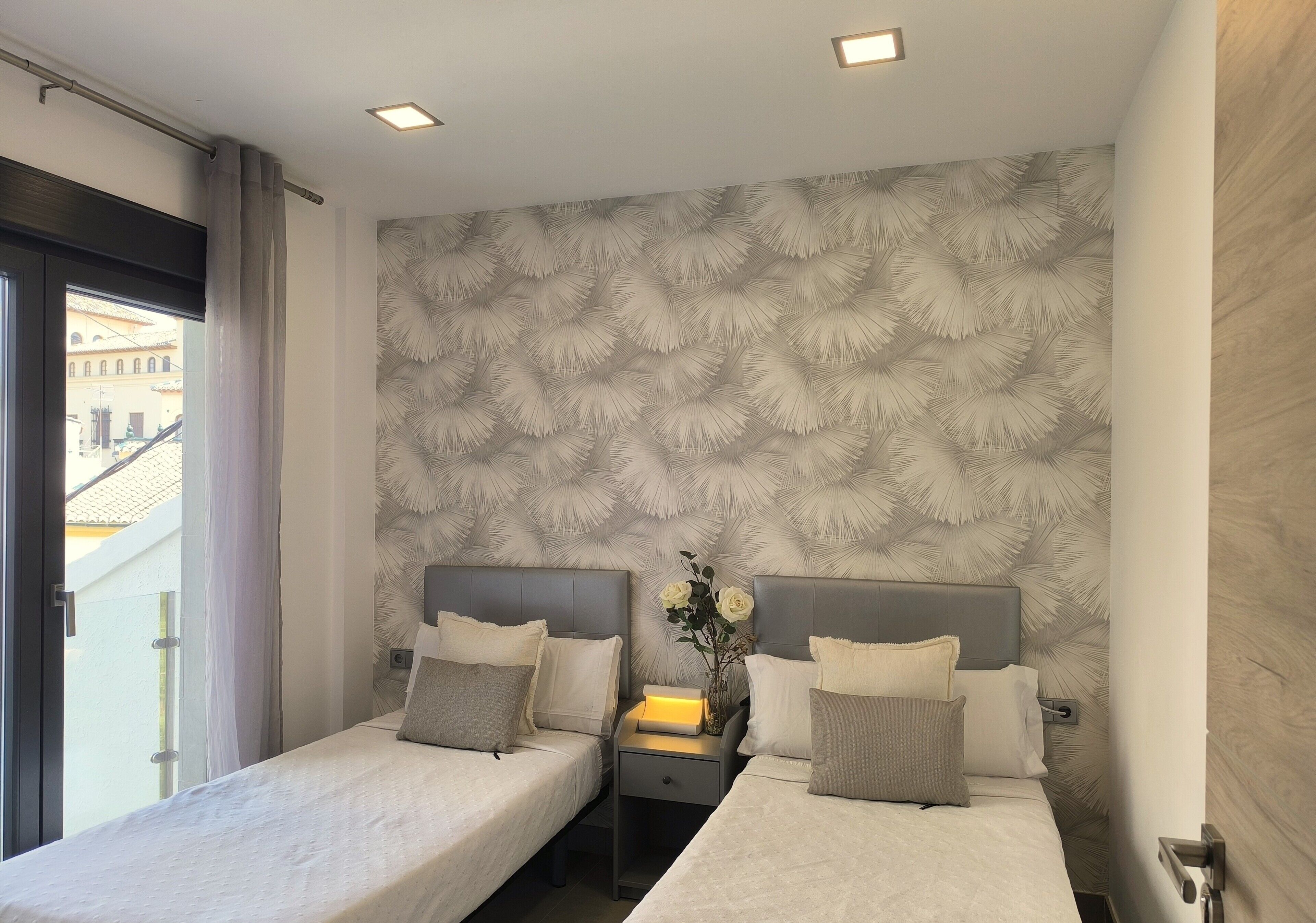 A hotel room with two beds, a nightstand with a lamp, and a patterned wall.