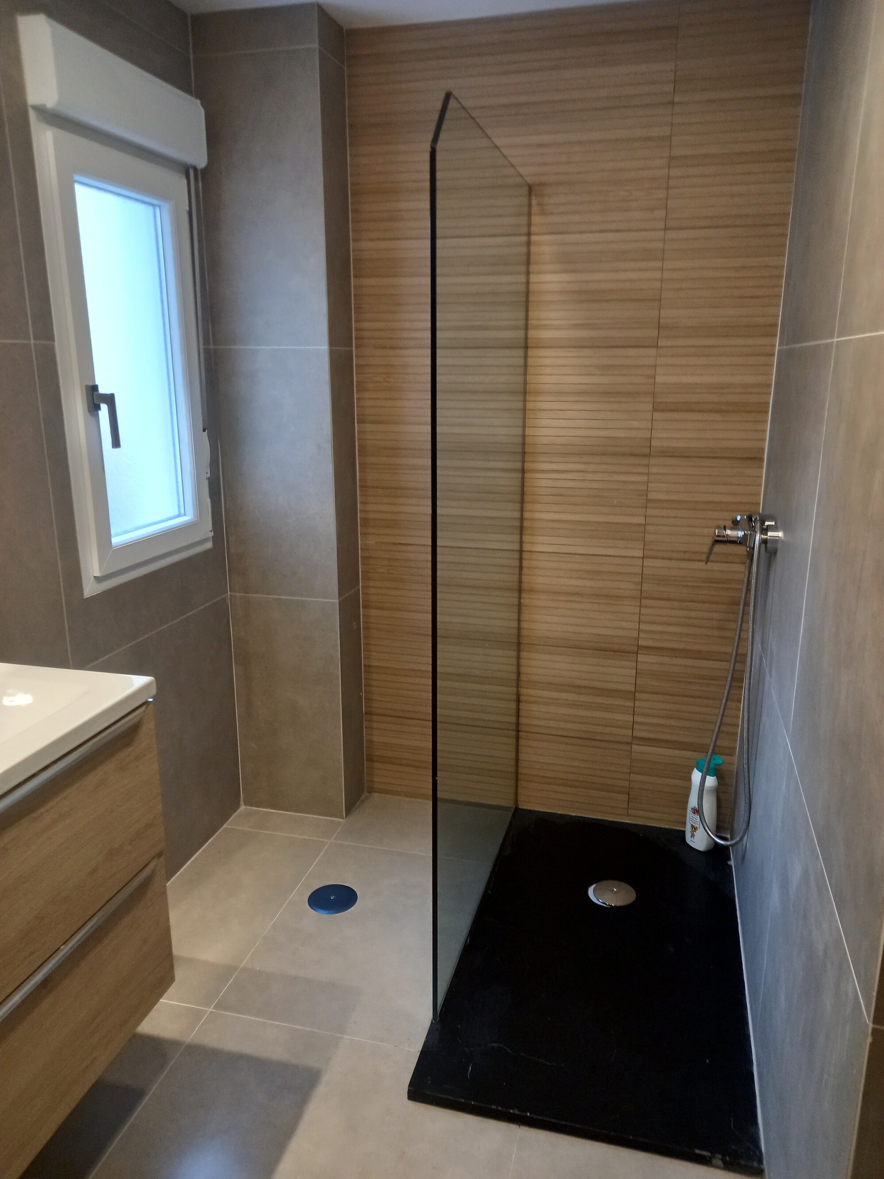 A modern bathroom with a shower, a window, and a sink.