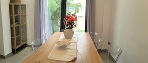 Un comedor con una mesa de madera, sillas transparentes, un florero con flores rojas y un aparador de vidrio.