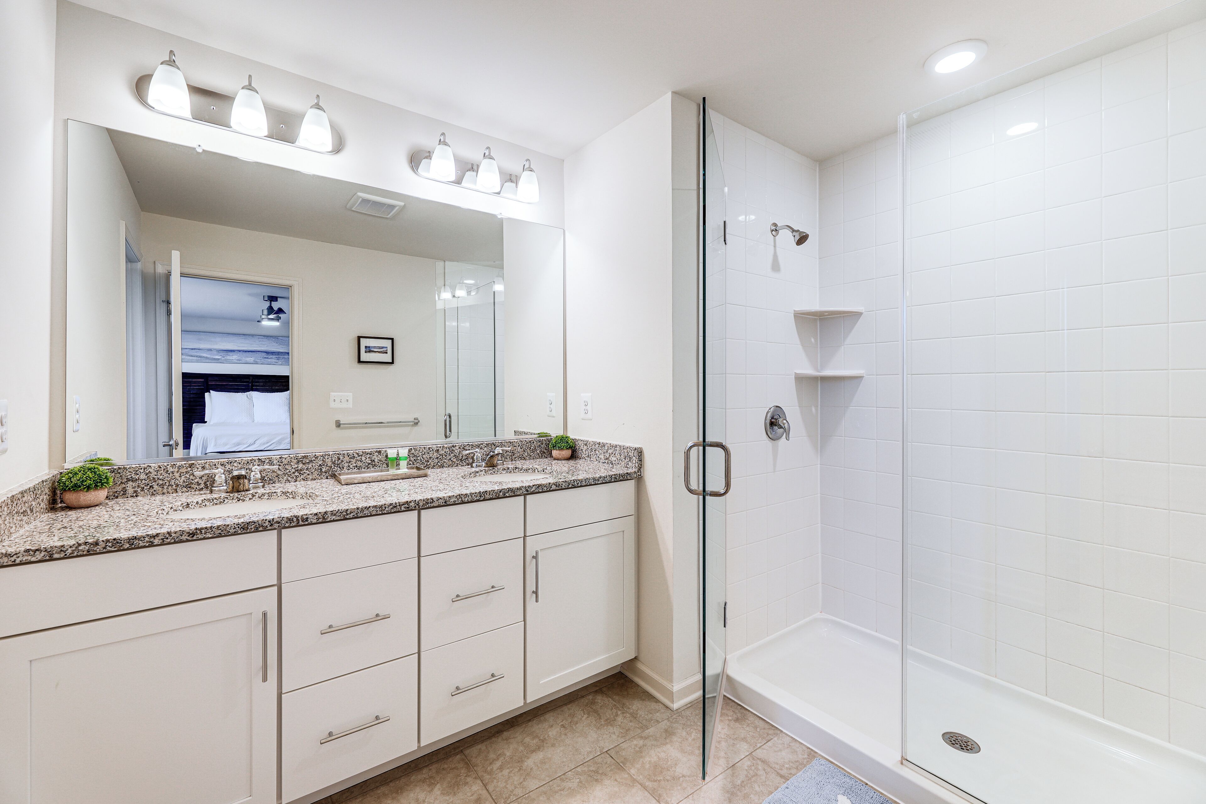 A modern bathroom with a glass-enclosed shower, a large mirror, and a granite countertop.