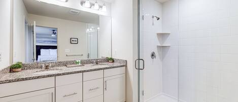 A modern bathroom with a glass-enclosed shower, a large mirror, and a granite countertop.