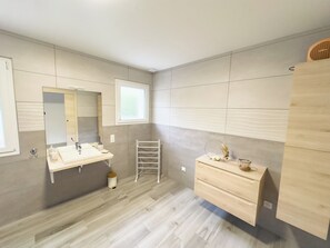 Une salle de bain moderne avec un grand miroir, un lavabo, un porte-serviettes et un meuble-lavabo en bois.