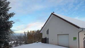 A snow-covered building with a garage, surrounded by trees and a clear sky. - New PMR-accessible gîte (Anould)