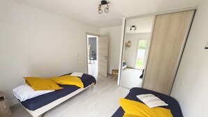 A room with two beds, each with yellow and white bedding, a wooden floor, and a large mirror on one wall. - New PMR-accessible gîte (Anould)