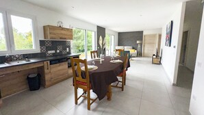 A modern kitchen with a dining area, large windows, and a view of greenery. - New PMR-accessible gîte (Anould)
