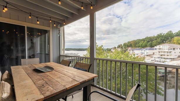 A wooden table with chairs on a balcony overlooking a river and buildings. - Close to the Pool- Great Family Condo- Screened in Porch- Lake Ozark (Lake Ozark)