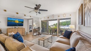 A modern living room with a ceiling fan, a TV, a sofa, a coffee table, and a balcony with a view of the neighborhood. - Close to the Pool- Great Family Condo- Screened in Porch- Lake Ozark (Lake Ozark)