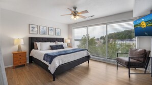 A bedroom with a bed, bedside tables, a ceiling fan, a large window with blinds, and a view of the city. - Close to the Pool- Great Family Condo- Screened in Porch- Lake Ozark (Lake Ozark)