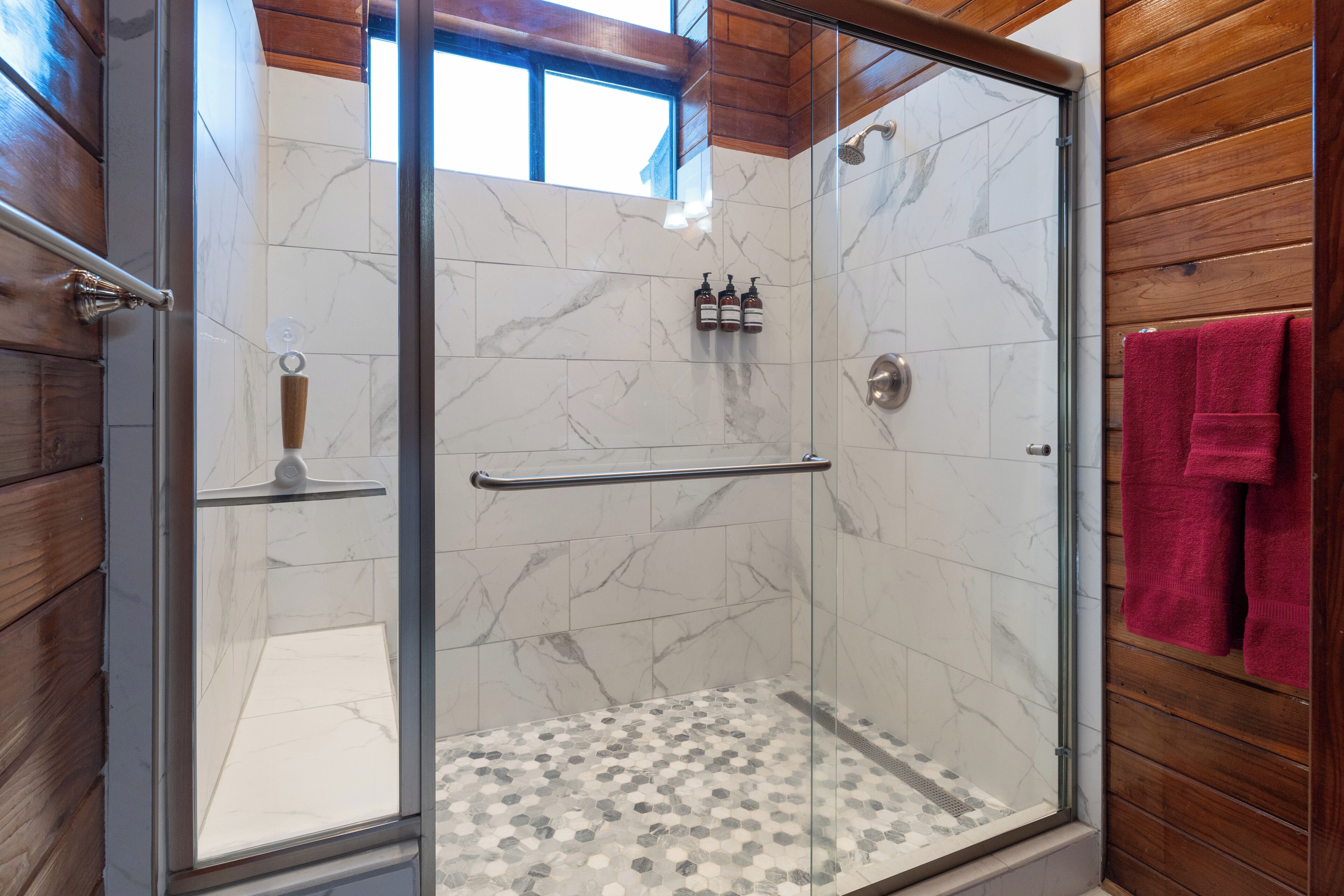 A glass-enclosed shower with marble tiles and a wooden interior.