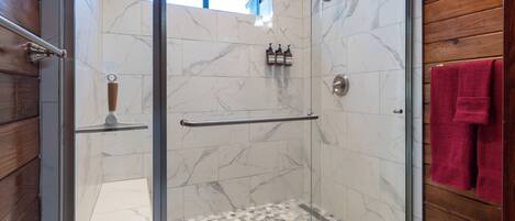 A glass-enclosed shower with marble tiles and a wooden interior.