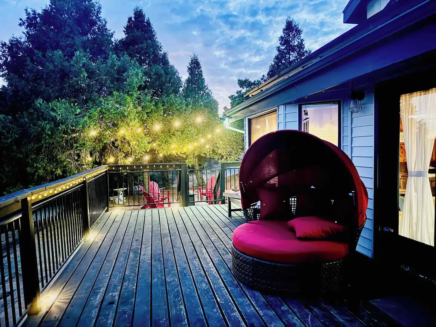 Een houten terras met een rode zithoek met kussens en sfeerverlichting.