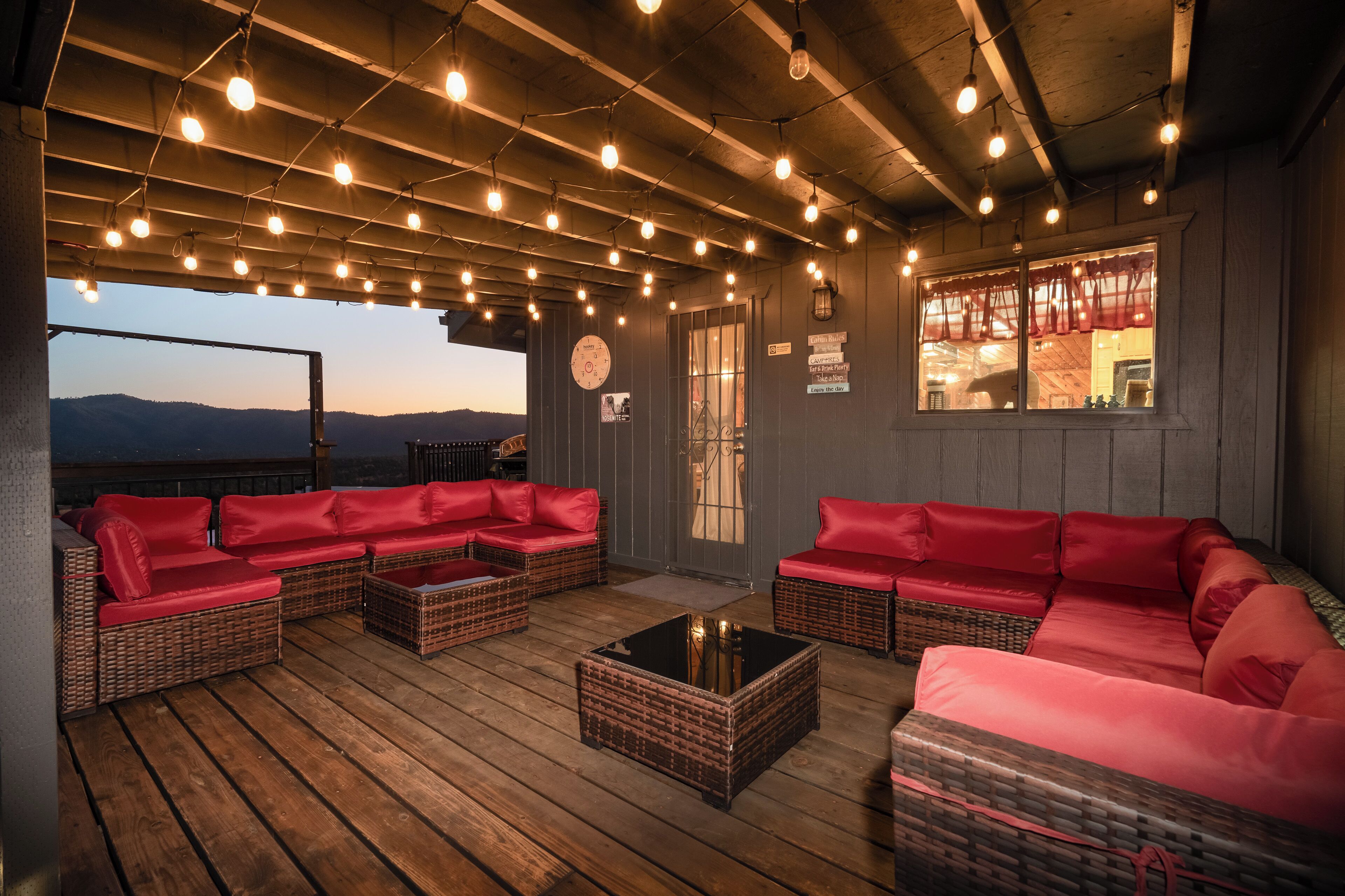 A cozy outdoor seating area with wicker furniture and red cushions, under a wooden ceiling with hanging lights.