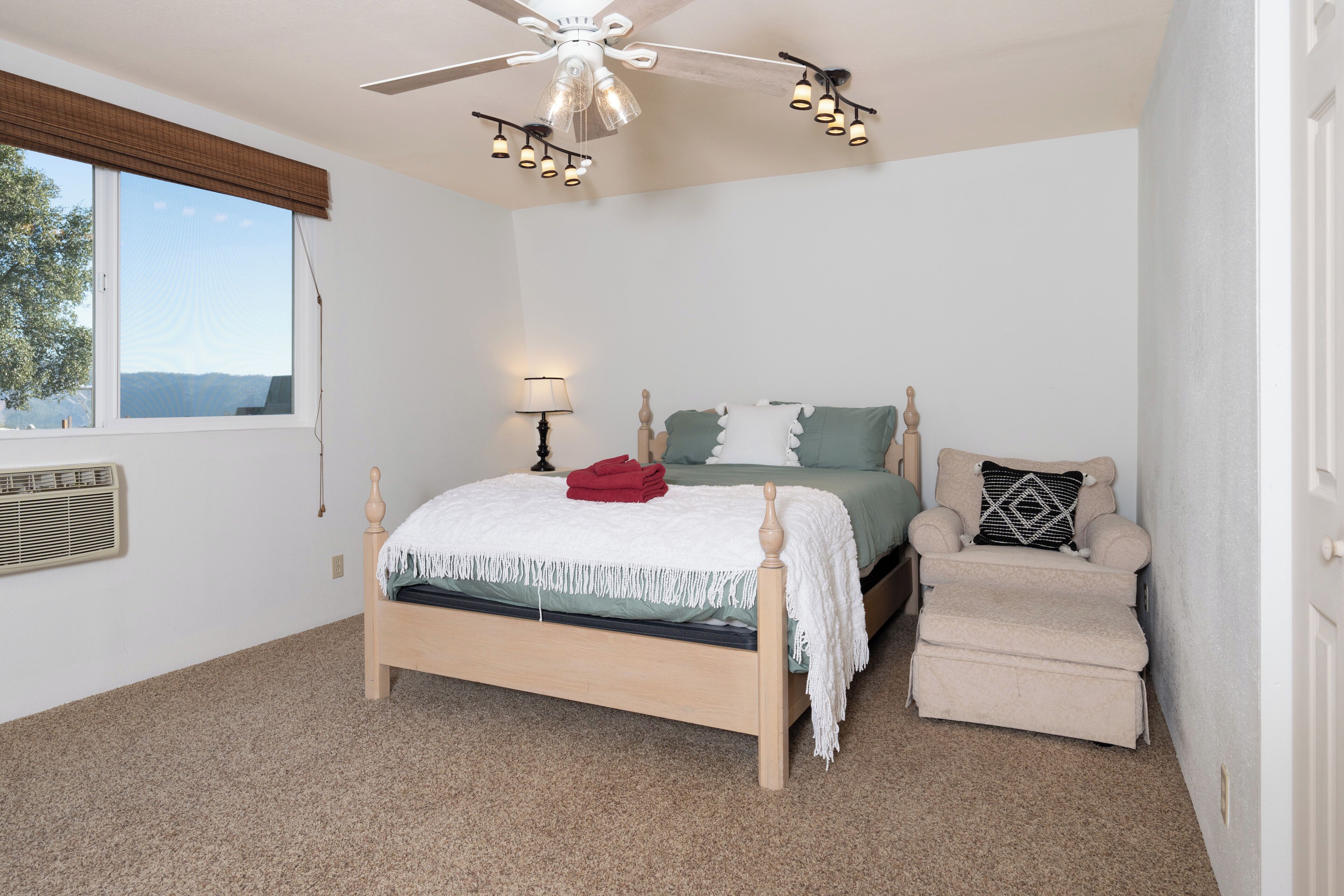 A bedroom with a bed, a chair, a ceiling fan, and a window.
