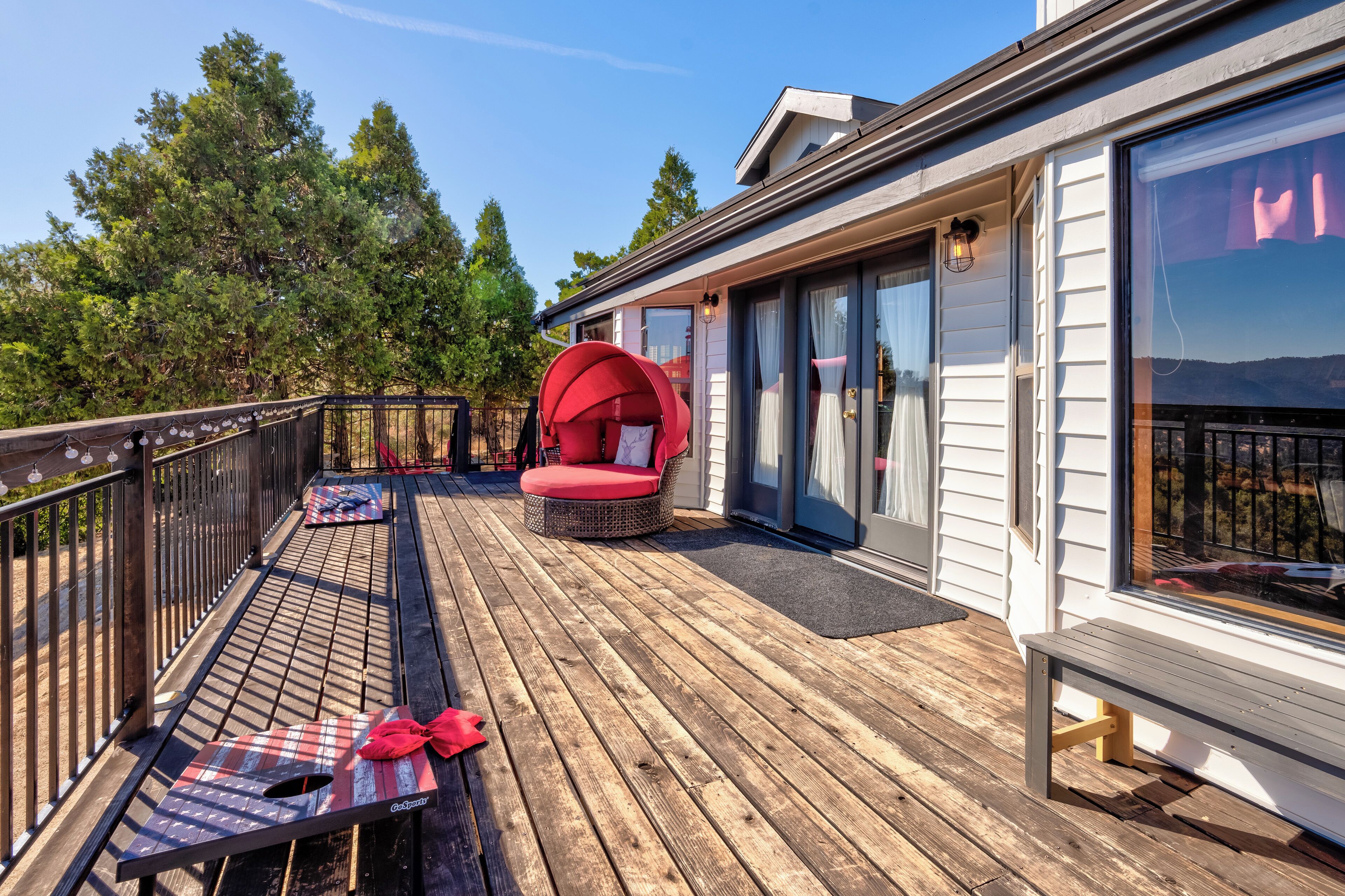 A wooden deck with a red chair and a bench, a railing, and a view of trees and a building.