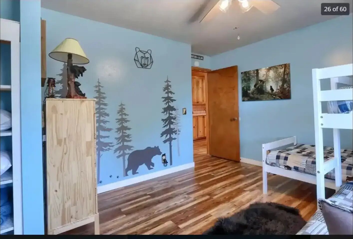 A room with a wooden wardrobe, a lamp, a bunk bed, and a wall mural of a bear and trees.