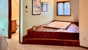 A bathroom with a wooden bench, a bathtub, and framed artwork on the wall.