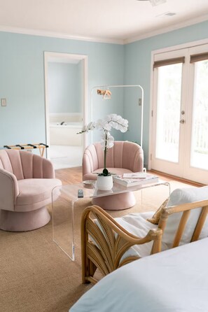 Una stanza con un letto, due sedie, un tavolo con un vaso di fiori, uno specchio e una finestra.