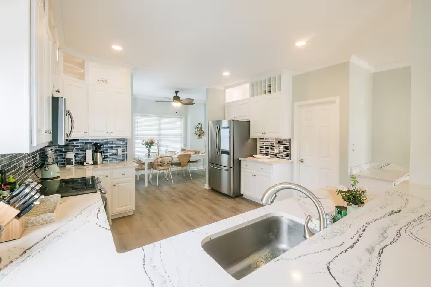 A modern kitchen with white cabinetry, a stainless steel refrigerator, and a marble countertop.