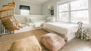Un dormitorio con una cama grande, una silla colgante, un perro y una ventana con vistas.