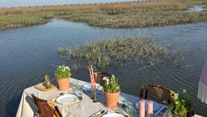 Una mesa de comedor dispuesta en un barco con sillas, rodeada de agua y humedales.